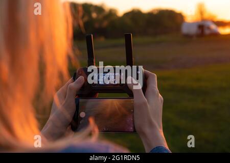 Ferngesteuerte Drohne in den Händen einer Frau Nahaufnahme auf dem Hintergrund des Sonnenuntergangs, Kopierraum. Foto hinter der Schulter Stockfoto