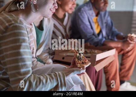 Nahaufnahme einer jungen Frau, die Pizza isst, während sie mit Freunden zu Hause Fernsehen, beleuchtet von blauem Licht, Kopierbereich Stockfoto