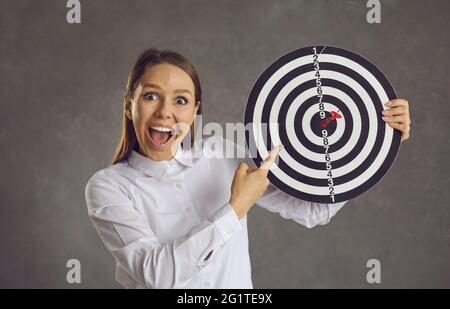 Porträt einer aufgeregten Geschäftsfrau, die mit dem Finger auf das Ziel zeigt, mit einem Pfeil direkt im Bullseye Stockfoto