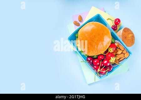 Zurück in die Schule, gesunde, leckere Lunchbox für Kinder mit Sandwiches, Nüssen, frischem Obst und Gemüsestöcken. Mit Schulbedarf, Bleistiften, Heften, auf bri Stockfoto