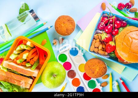 Zurück in die Schule, gesunde, leckere Lunchbox für Kinder mit Sandwiches, Nüssen, frischem Obst und Gemüsestöcken. Mit Schulbedarf, Bleistiften, Heften, auf bri Stockfoto