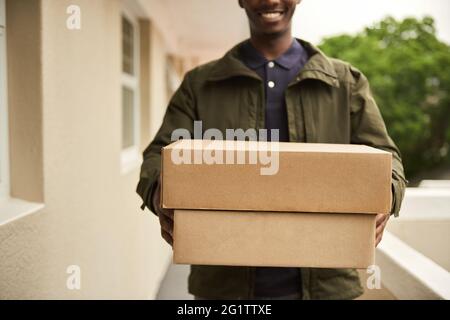 Lächelnder afrikanischer Lieferer, der Pakete zum Haus eines Kunden trägt Stockfoto
