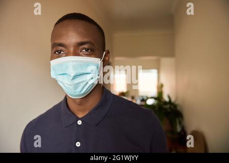 Junger afrikanischer Mann, der zu Hause eine schützende Gesichtsmaske trägt Stockfoto