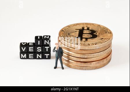 Würfel mit INVESTITIONSTEXT auf weißem Hintergrund. Geschäftsmann Figur denken in der Nähe von Würfeln mit Investition Wort, während in der Nähe Bitcoin Stapel stehen. Stockfoto