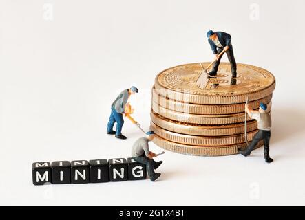 Gruppe von Bergarbeiterfiguren mit Ausrüstung, die an einem Stapel von Bitcoins in der Nähe von schwarzen Würfeln mit MINING-Text arbeitet. Stockfoto