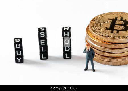 Schwarze Würfel mit BUY, SELL und HODL Text auf weißem Hintergrund. Denken Geschäftsmann Figur Blick auf Würfel, während lehnte sich an Bitcoin-Stapel. Stockfoto