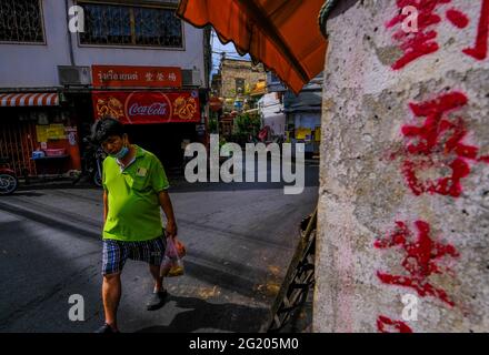 Ein Mann geht entlang einer schmalen, sonnendurchfluteten Straße in Talat Noi, Bangkok, Thailand Stockfoto