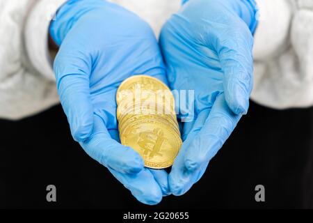 Nahaufnahme Frau Hand in Gummihandschuhe halten Gold Bitcoin Münzen. Stockfoto