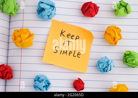 Halten Sie es einfach. Eine gelbe Papiernote mit der Phrase halten Sie es einfach auf sie mit einigen bunten zerknitterten Papierkugeln um sie herum. Nahaufnahme. Stockfoto