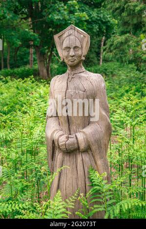 Nocton, Lincolnshire, England, Großbritannien. Eine alte geschnitzte Holzfigur einer Frau im Wald zwischen überwucherten grünen Bracken Stockfoto