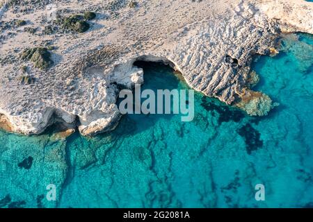 Griechenland. Kykladen. Seascape mit Höhlen und Felsen über grünem smaragdklarem Meerwasser, kleine Kykladen-Insel, Luftdrohne von oben nach unten Stockfoto