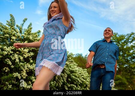 Paar läuft im Frühling blühenden Park. Junge Männer und Frauen, die sich beim Sonnenuntergang amüsieren. Stockfoto