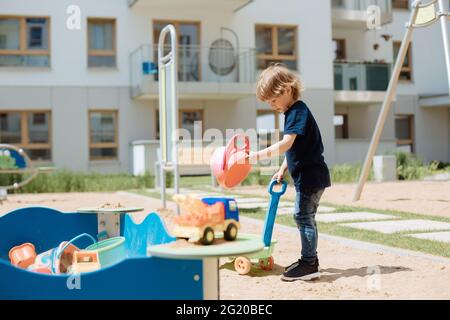 Das 3-jährige Kind spielt auf dem offenen Spielplatz im Hof mit Spielzeug. Freizeitkonzept für Kinder Stockfoto