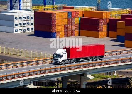 Containerschiff LKW Autotransport von Containern auf der Autobahnbrücke im Hintergrund ein Seehafen mit einem Lager von Containern Hof exportiert Stockfoto