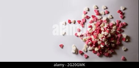 Süße Herzen. Rosa, rote und weiße herzförmige Zuckerstreuseln. Buntes Herz aus vielen kleinen Herzen. Valentinstag oder Muttertag Hintergrund Stockfoto
