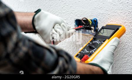 Elektriker bei der Arbeit mit dem Tester misst die Spannung in einem elektrischen System. Sicheres Arbeiten mit Schutzhandschuhen. Bauindustrie. Stockfoto