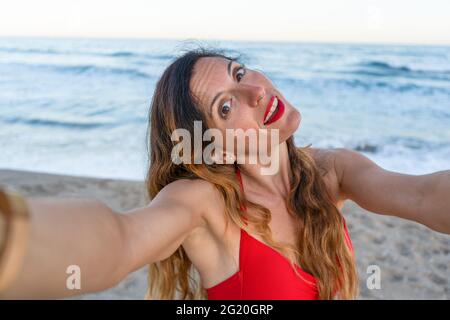 Schöne junge Frau, die Spaß hat, ein Selfie am Strand bei Sonnenuntergang zu machen. Stockfoto