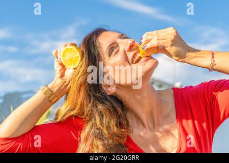 Porträt einer glücklichen Frau, die Zitrone im roten T-Shirt isst. Stockfoto