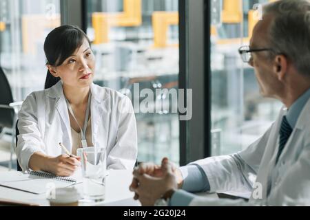 Porträt einer asiatischen Ärztin, die während eines medizinischen Meetings im Konferenzraum mit Kollegen spricht Stockfoto