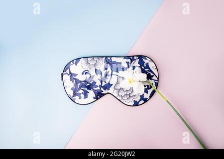 Schöne Seidenschlaf-Maske für die Augen mit Blumenmuster und weißen Narzissen oder Narzissen Blume auf einem rosa blauen Hintergrund Stockfoto