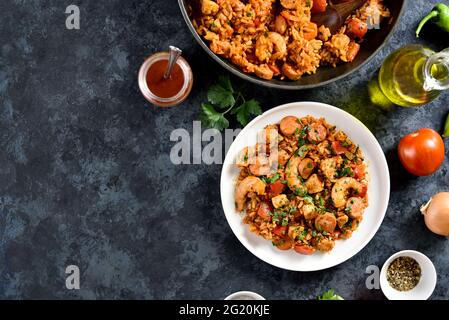 Kreolisches Jambalaya mit Reis, geräucherten Würstchen, Hühnerfleisch und Gemüse auf dem Teller auf blauem Stein-Hintergrund mit Kopierfläche. Draufsicht, flach liegend Stockfoto