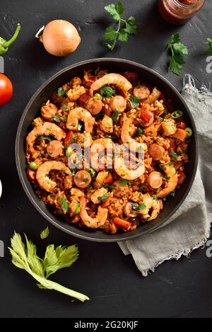 Kreolischer Stil Jambalaya mit Huhn, geräucherten Würstchen und Gemüse in Bratpfanne auf schwarzem Stein Hintergrund. Draufsicht, flach liegend, Nahaufnahme Stockfoto