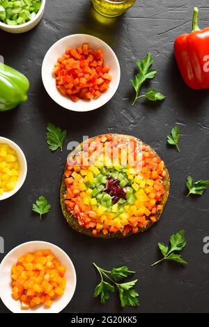 Rainbow Veggie Paprika Pizza auf schwarzem Stein Hintergrund. Vegetarisch vegan oder gesundes Essen Konzept. Glutenfreie Diät Gericht. Draufsicht, flaches Lay Stockfoto