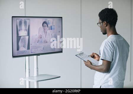 Rückansicht eines afroamerikanischen Arztes, der mit einer Expertin per Videoanruf in der Klinik spricht, Raum kopieren Stockfoto