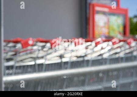 Verschwommene Einkaufswagen mit roten Griffen. Seitenansicht einer Reihe mit mehreren Schubkarren. Alles außer Fokus. Deutschland Stockfoto