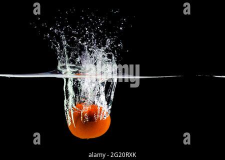 Mandarin fällt ins Wasser und erzeugt auf schwarzem Hintergrund Spray, Kopierfläche Stockfoto