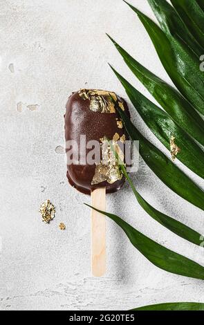 Die mit Schokolade überzogenen Eiszapfen mit einem Blatt essbaren Goldes auf einem hellen Betongrund. Popsicle und süßes Dessert auf einem Stock. Selektiv Stockfoto