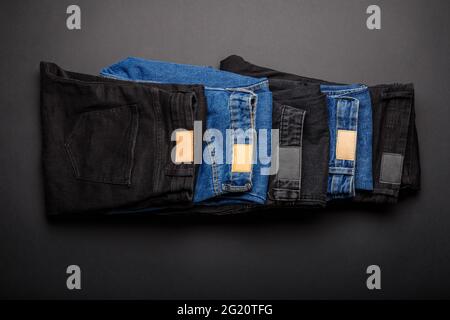 Jeans in Denim-Blau und schwarze jeans im Stapel auf schwarzem Hintergrund Draufsicht. Jeans jeans hose tragen im Stapel gefaltet. Stockfoto