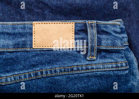 Braunes, lederfarbenes Etikett auf Denim-Hosen-Hintergrund. Leeres Mockup-Etikett in beigem Leder. Jeans in blauer Denim mit Emty-Label. Nahaufnahme Stockfoto