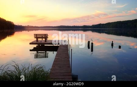 Bank auf einem hölzernen Pier bei Sonnenuntergang, Lipie Lake in Dlugie Village, Polen Stockfoto