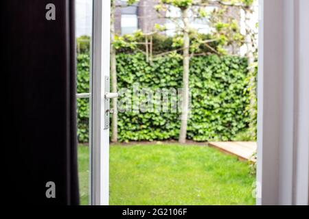 Nahaufnahme halb geöffnete moderne Türöffnung mit verschwommenem grünen Gartenhintergrund im Sommer des modernen Hauses Stockfoto