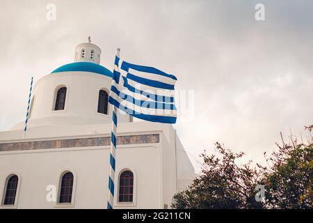 Santorini Ansicht der Kirche mit blauer Kuppel und griechischer Flagge in Oia, Griechenland. Tourismus, Reisen, Sommerurlaub. Traditionelle Architektur Stockfoto