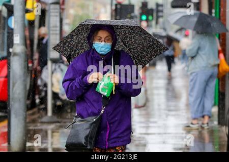 London, Großbritannien. Juni 2021. Eine Frau, die eine Gesichtsmaske trägt, schützt sich während eines Regenfalls in London unter einem Regenschirm vor dem Regen. Kredit: SOPA Images Limited/Alamy Live Nachrichten Stockfoto