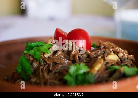 soba-Pasta mit Tomaten und Kräutern auf einer Keramikplatte in einem öffentlichen Speisesaal, Vorder- und Hintergrund verschwommen mit Bokeh-Effekt Stockfoto