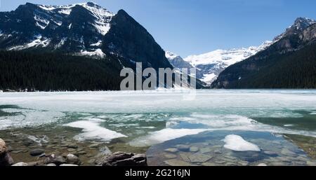 Wunderschöner Blick auf Lake Louise, der im Frühling schmilzt. Frost auf der Oberfläche des Sees, verschneite Berge. Sonniger Tag mit blauem Himmel. Banff-Nationalpark, Stockfoto