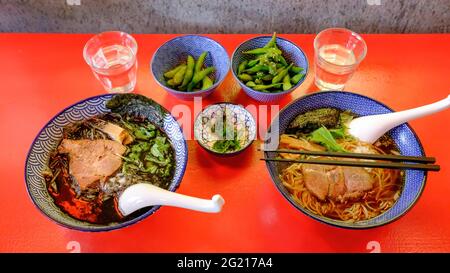 Bild von zwei Schalen Ramen (japanische heiße Suppe), serviert in schönen blau bemalten Schalen auf einem leuchtend roten Tisch. Stockfoto
