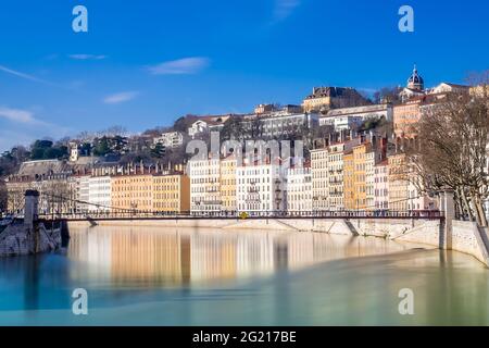 Winterszene des Flusses Saone in Lyon, Frankreich, die das warme Licht der weißen und gelben Gebäude am Ufer reflektiert und von einer Fußgängerbrücke überquert wird Stockfoto