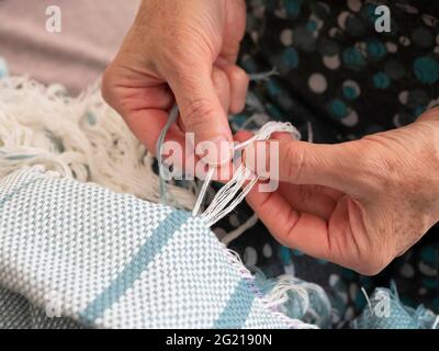 Eine ältere Frau bildet einen Rand auf einem gewebten Schal. Hände des Handwerkers bei der Arbeit Stockfoto