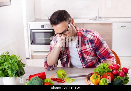 Gemüse Tomaten Paprika Radieschen auf dem Tisch. Aufgeregter Mann, der auf dem Ellenbogen sitzt und hackt. Stockfoto