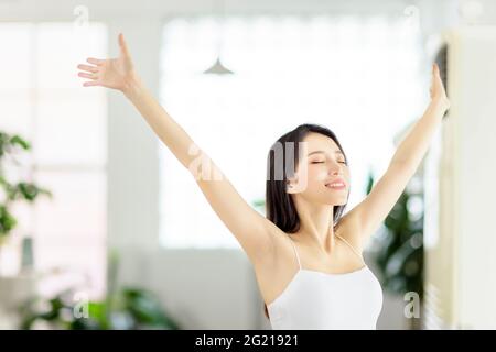 Schöne asiatische junge Frau, die einen tiefen Atemzug im Wohnzimmer Stockfoto