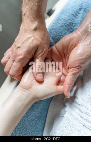 Nahaufnahme der Hände eines unbekannten kaukasischen Therapeuten, der die Hände einer unbekannten Kundin massiert und dehnt Stockfoto