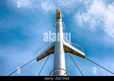 Der Mast eines modernen Schiffes vor dem Hintergrund des blauen Himmels. Mast des Bootes, Ansicht von unten, Detail des Segelbootes Stockfoto