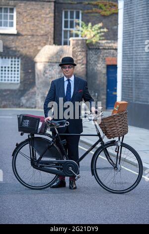 Kleine Straße in London ein Geschäftsmann, der neben dem Pashley Guvnor Fahrrad steht und einen Anzug mit Melone und Krawatte trägt. Stockfoto