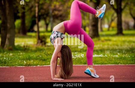 Junge Frau dehnt sich vor dem Fitnesstraining im Park. Gesunde junge Frau, die sich im Freien aufwärmt. Sie streckt ihre Arme Stockfoto