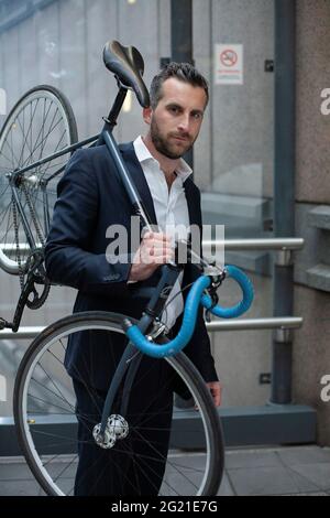 Kaukasischer Geschäftsmann, der Fahrrad auf der Schulter trägt Stockfoto