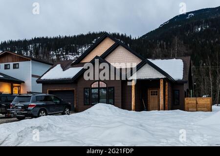 REVELSTOKE, KANADA - 14. MÄRZ 2021: Privathaus und Straßenansicht in Kleinstadt Abendzeit früher Frühling mit Schnee Stockfoto